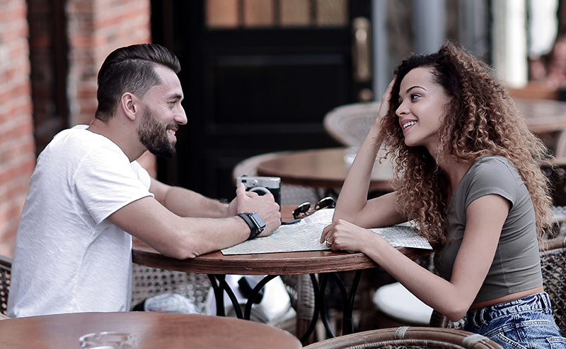 Young couple eating a meal together outside smiling.